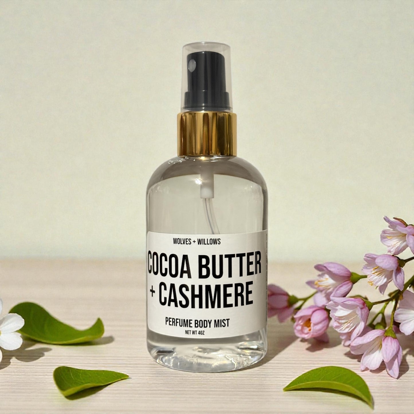 Perfume body mist bottle labeled 'Cocoa Butter + Cashmere' with flowers and leaves on a light background