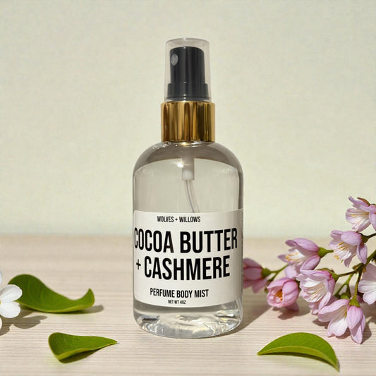 Perfume body mist bottle labeled 'Cocoa Butter + Cashmere' with flowers and leaves on a light background