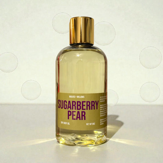 Bottle of 'Sugarberry Pear' dry body oil with a gold cap on a light background