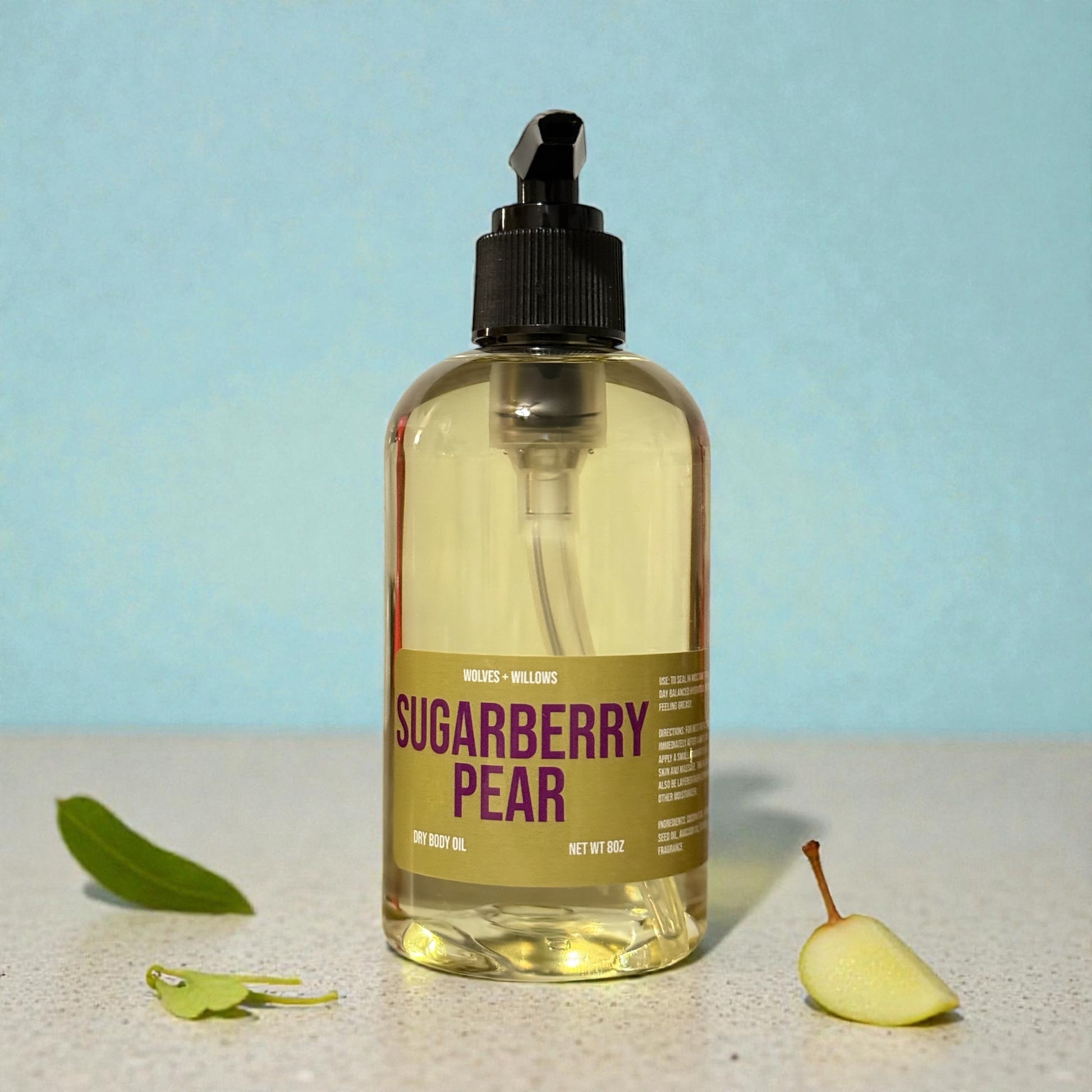 Bottle of 'Sugarberry Pear' body oil with a label on a light blue background