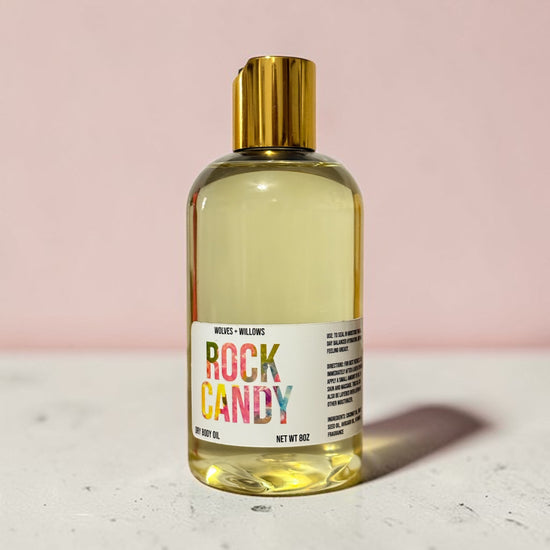 Bottle of 'Rock Candy' body oil with a gold cap on a light pink background