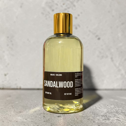 Bottle of sandalwood body oil with a gold cap on a textured surface.