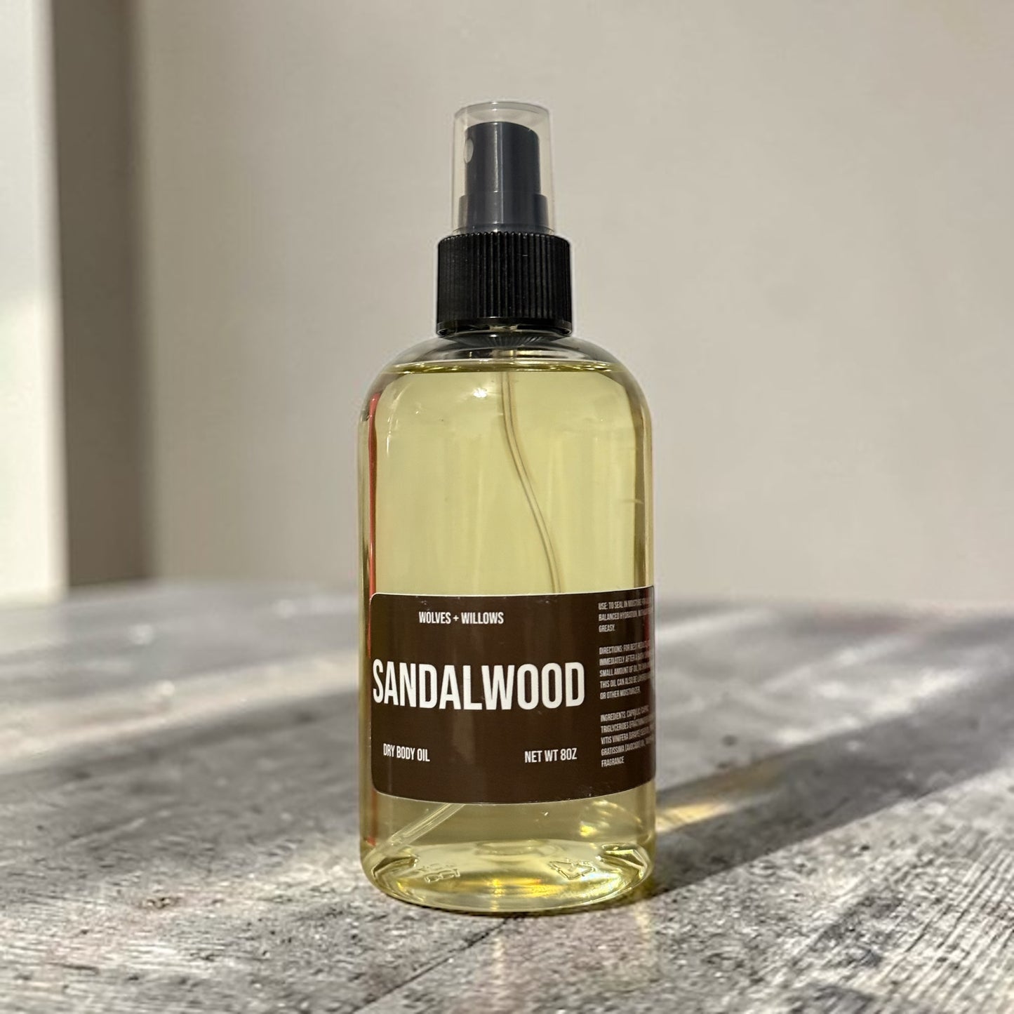 Bottle of sandalwood body oil on a wooden surface with a neutral background
