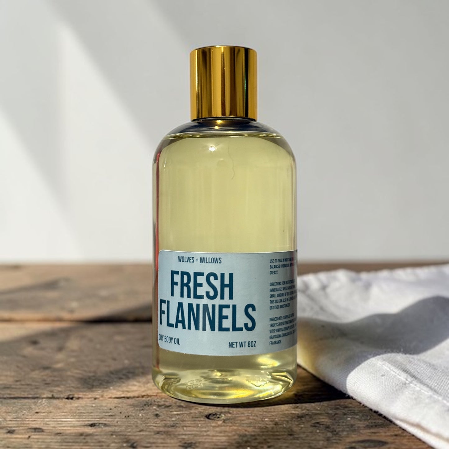 Bottle of 'Fresh Flannels' body oil on a wooden surface with a white towel.