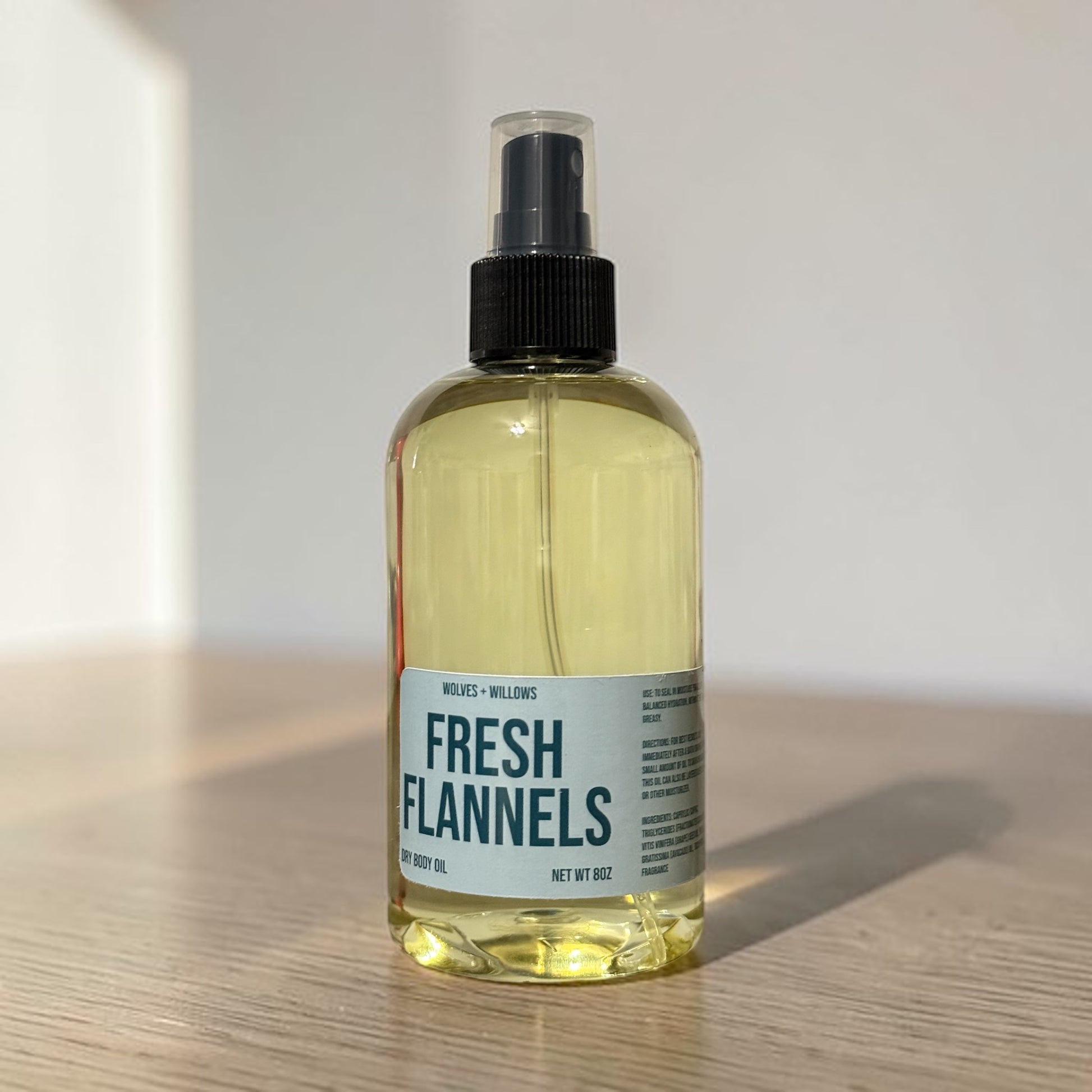Bottle of 'Fresh Flannels' body oil on a wooden surface with a neutral background