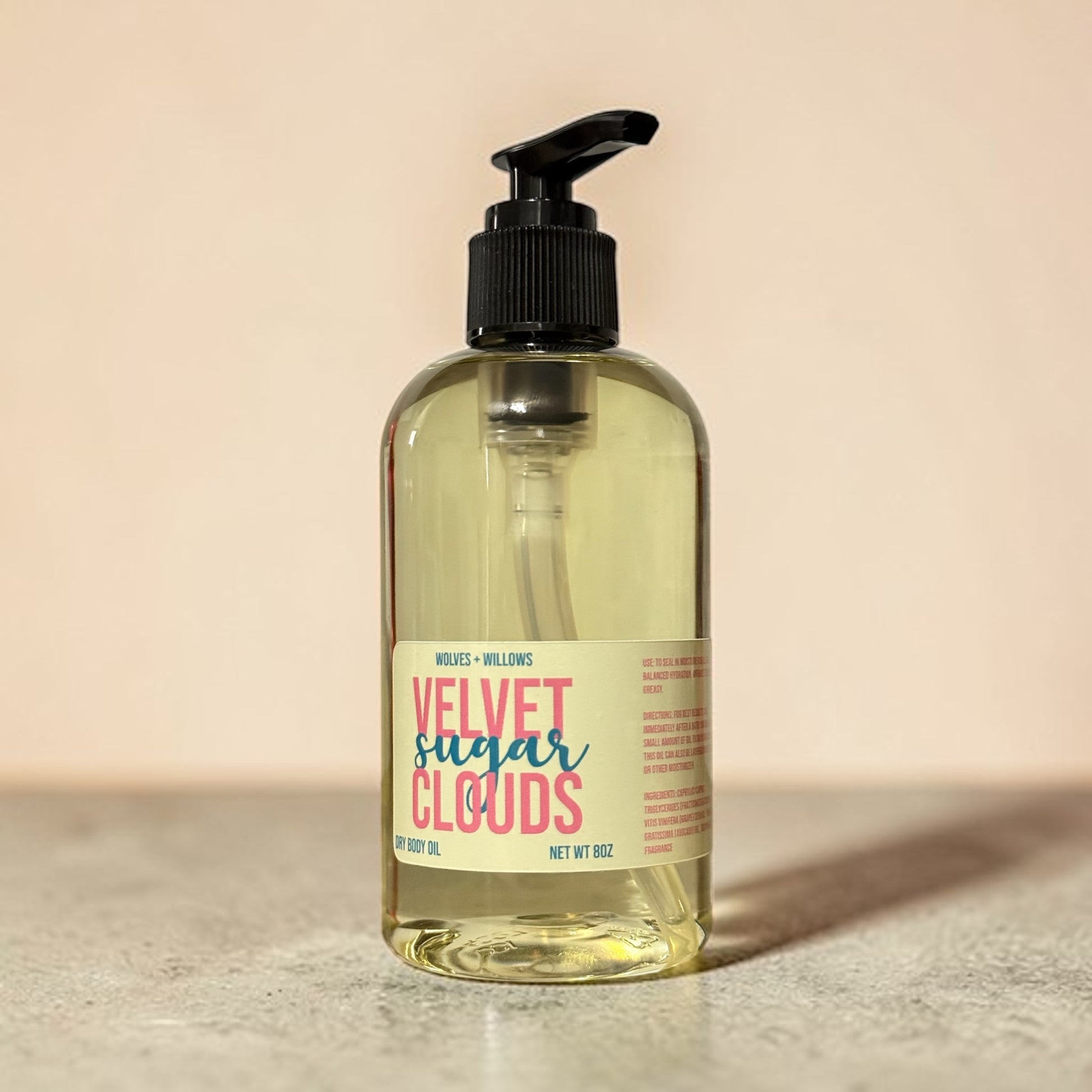 Bottle of 'Velvet Sugar Clouds' body oil with a pump on a beige background