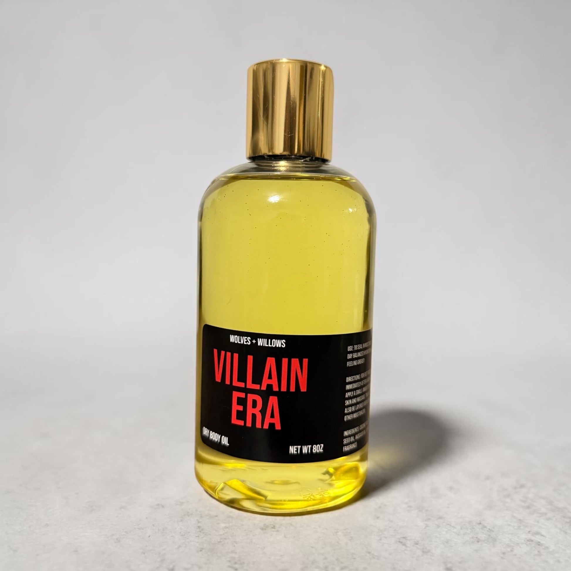 Bottle of 'Villain Era' body oil with a gold cap on a light gray background