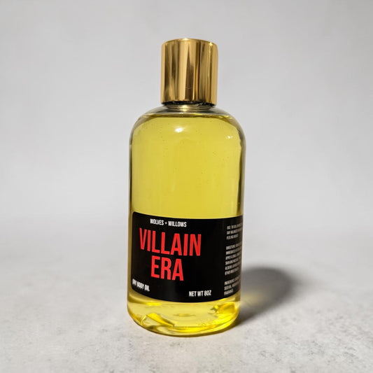 Bottle of 'Villain Era' body oil with a gold cap on a light gray background