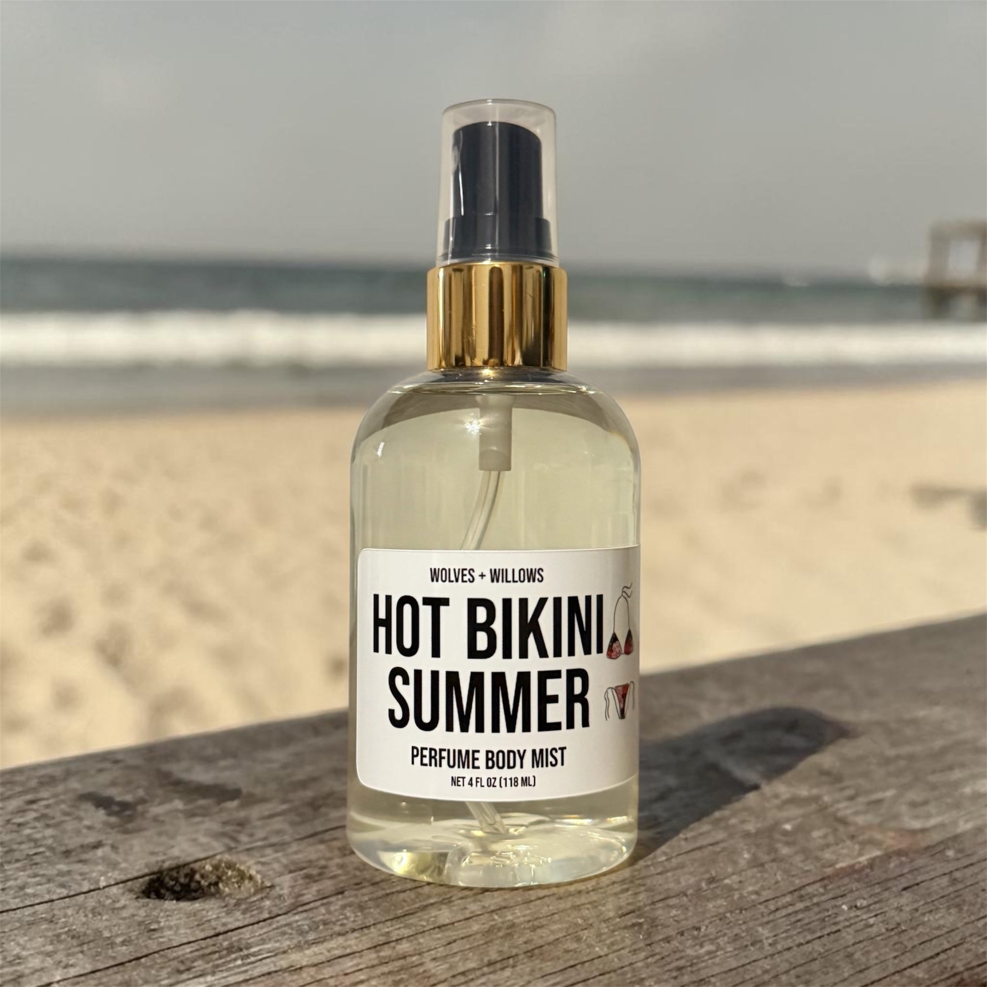 Bottle of 'Hot Bikini Summer' perfume body mist on a wooden surface with a beach background