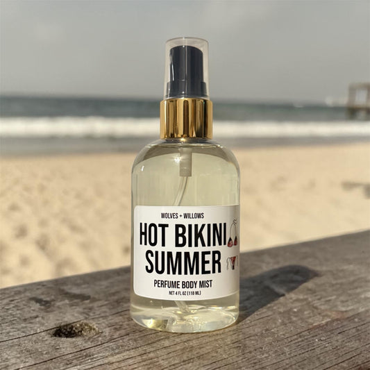 Bottle of 'Hot Bikini Summer' perfume body mist on a wooden surface with a beach background