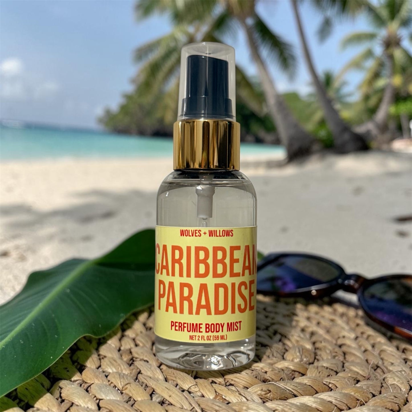 Perfume body mist bottle labeled 'Caribbean Paradise' on a beach setting with palm trees and sand.