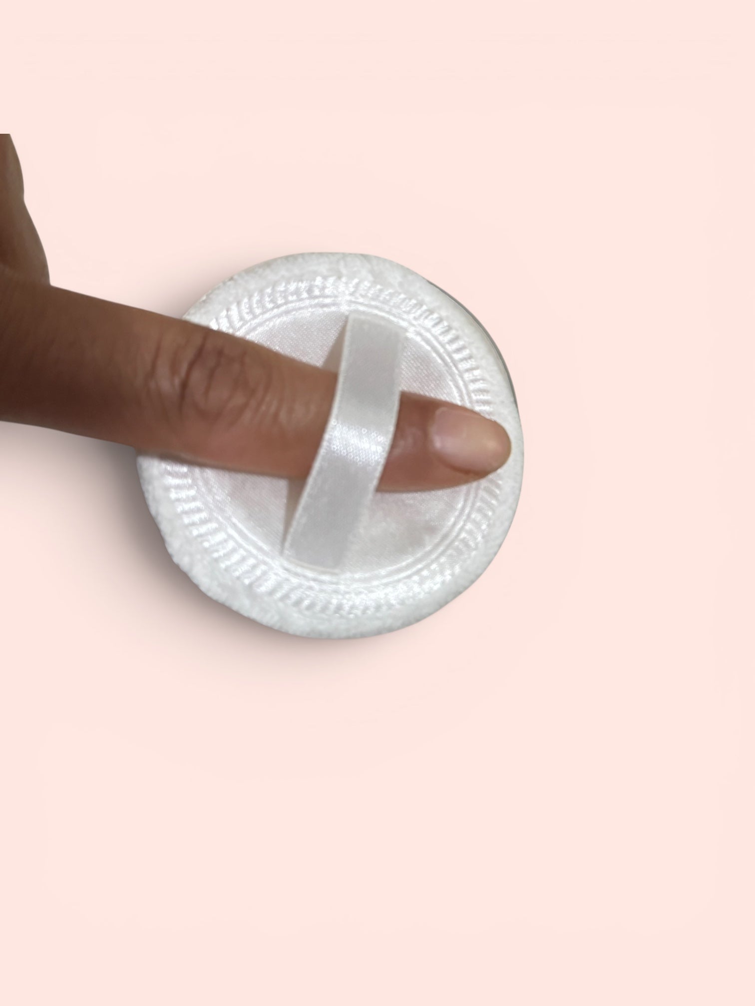 White circular object with a ribbon being wrapped around it, on a pink background