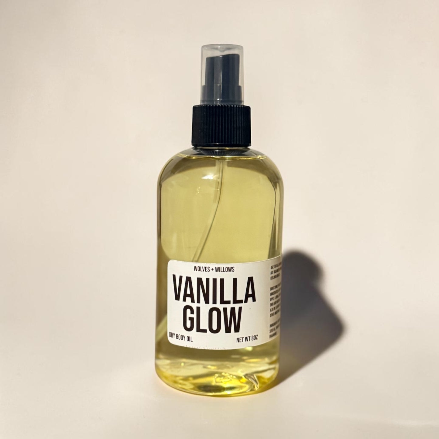 Bottle of Vanilla Glow body oil with a black spray nozzle on a beige background
