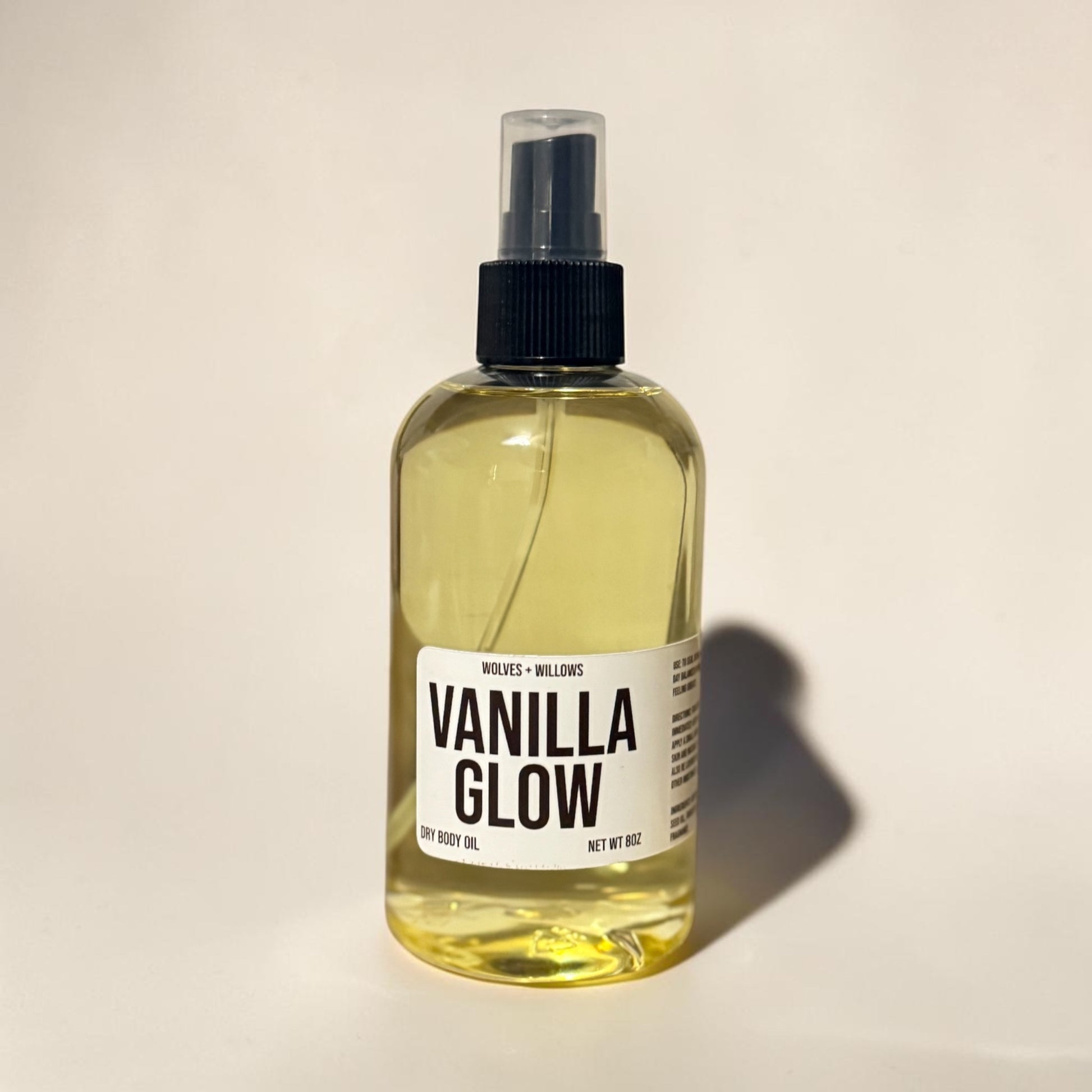 Bottle of Vanilla Glow body oil with a black spray nozzle on a beige background