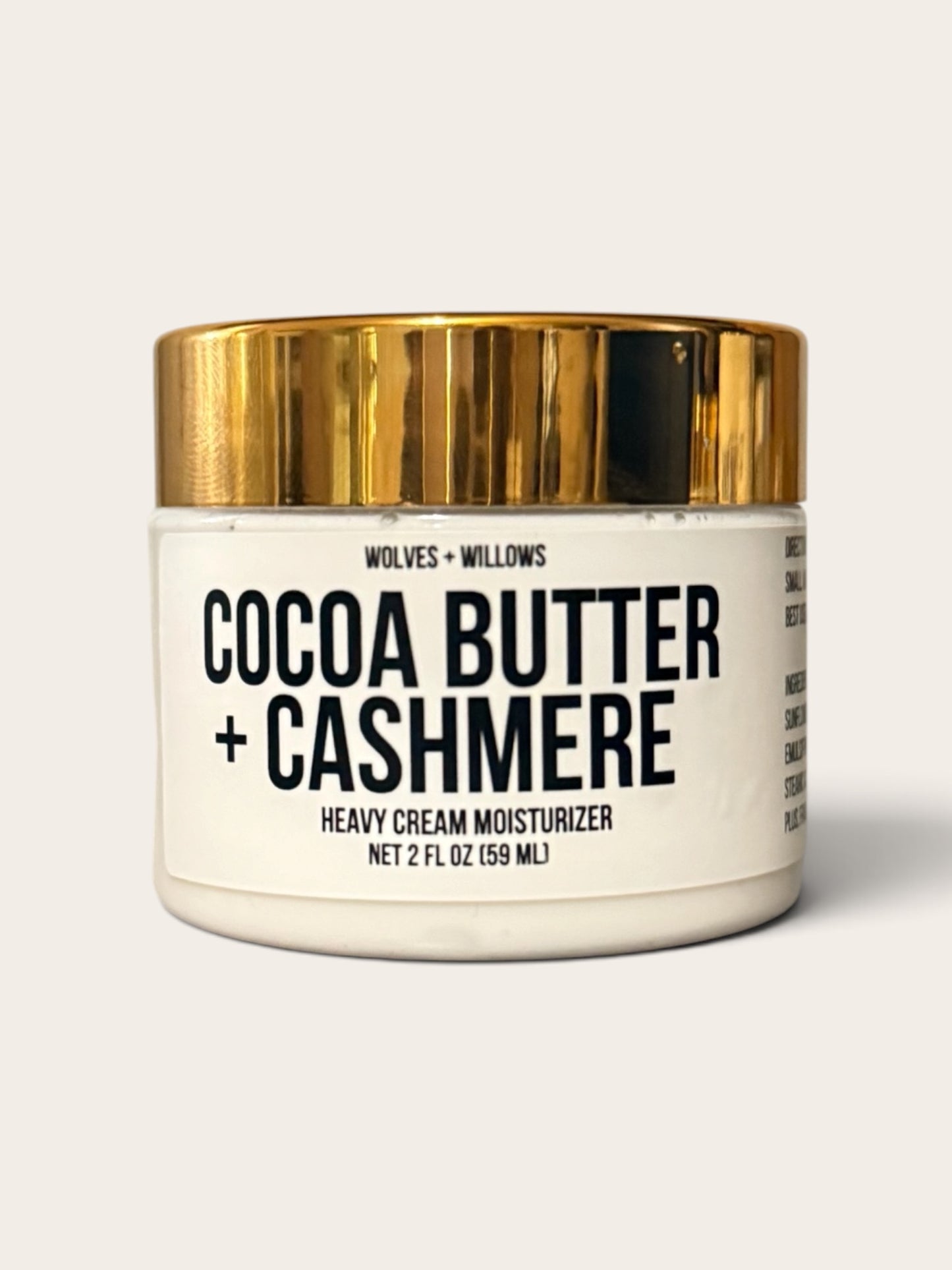A jar of Wolves + Willows Cocoa Butter + Cashmere heavy cream moisturizer, featuring a white jar with a metallic gold lid and black text, set against a light beige background.