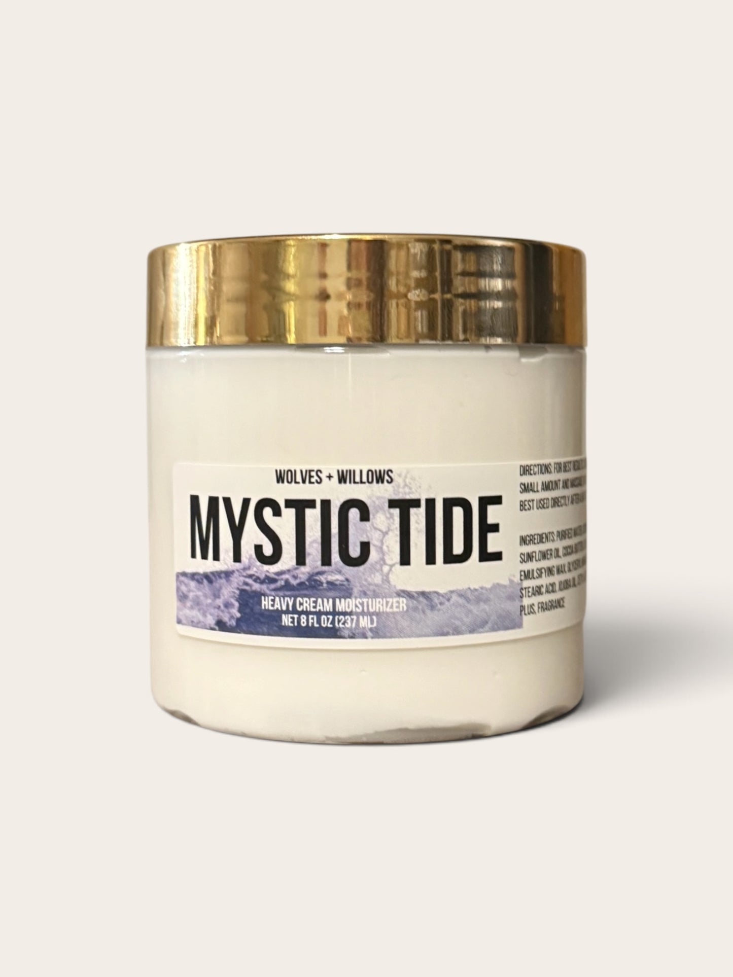 A jar of Wolves + Willows Mystic Tide Heavy Cream Moisturizer with a gold metallic lid and a white label featuring black text and a blue-purple graphic, set against a light beige background.