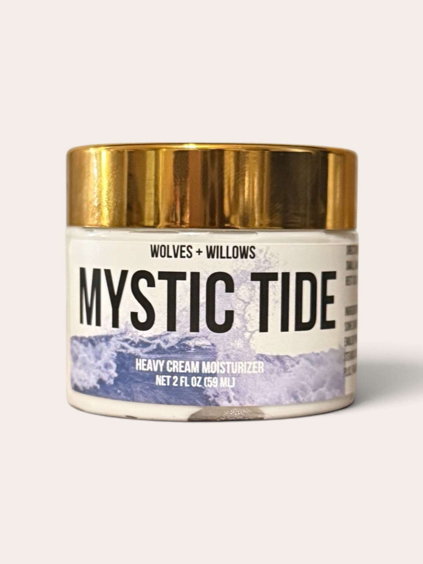 A jar of Wolves + Willows Mystic Tide Heavy Cream Moisturizer with a metallic gold lid and a white label featuring a purple ocean graphic, set against a light beige background.