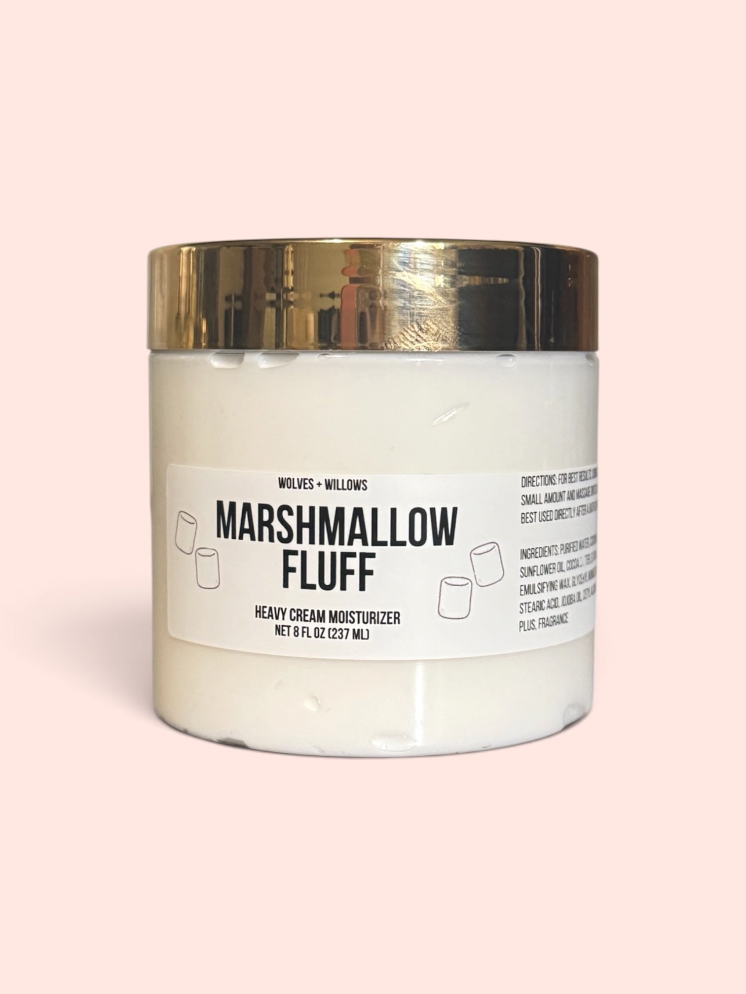 Marshmallow Fluff Heavy Cream Moisturizer by Wolves + Willows in a white jar with a metallic gold lid, set against a solid pale pink background.