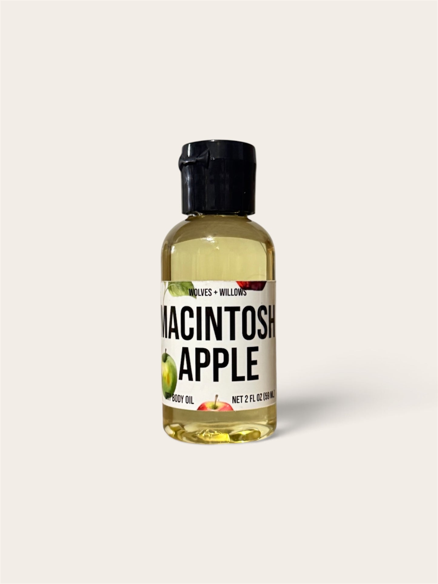 A 2 fl oz bottle of Wildcreek Naturals Macintosh Apple Foot Oil, featuring a clear bottle filled with pale yellow oil, a black cap, and a white label with green and red apple illustrations, set against a solid off-white background.