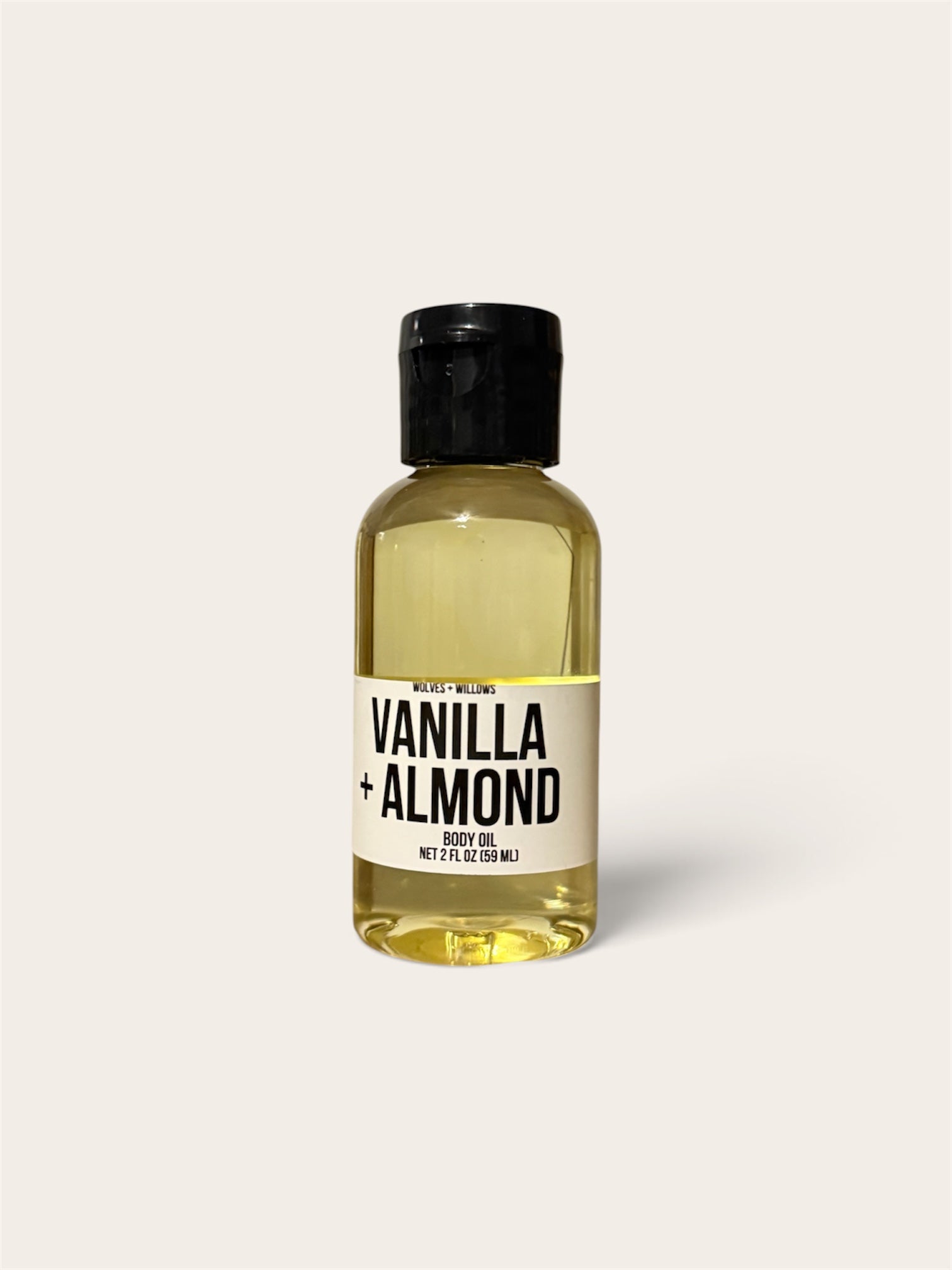 A 2 fl oz body oil bottle with a black cap and a cream label reading 'VANILLA + ALMOND' on a light beige background.