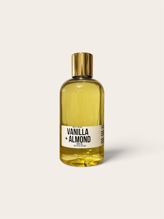 A clear bottle filled with pale yellow liquid, featuring a metallic gold cap and a white label that reads 'VANILLA + ALMOND'. The bottle is centered against a solid, warm off-white background.