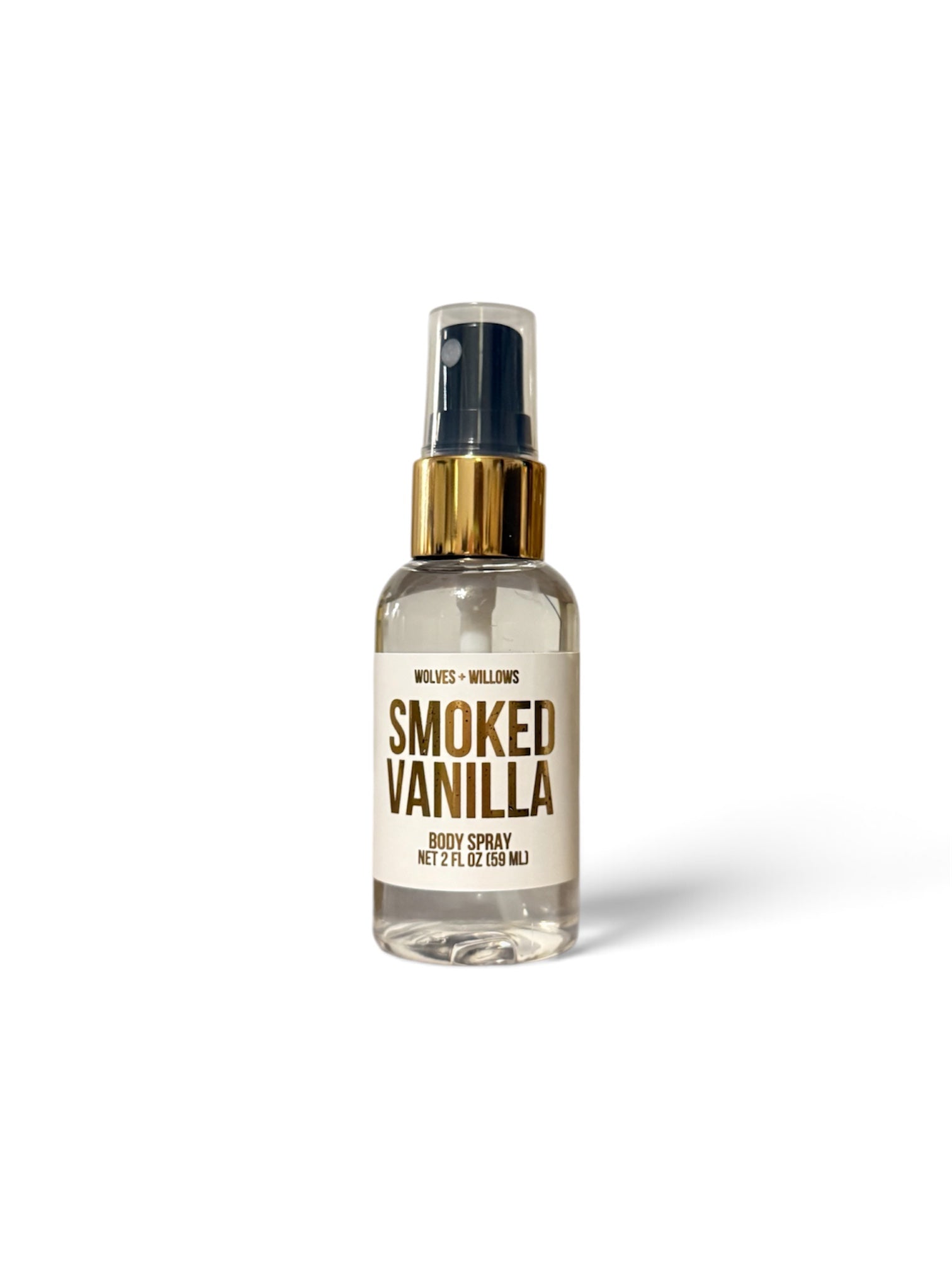A 2 fl oz body spray bottle with a clear glass body, cream-colored label, gold collar, and a dark navy spray nozzle, labeled 'SMOKED VANILLA' by Wilies + Wiliness.