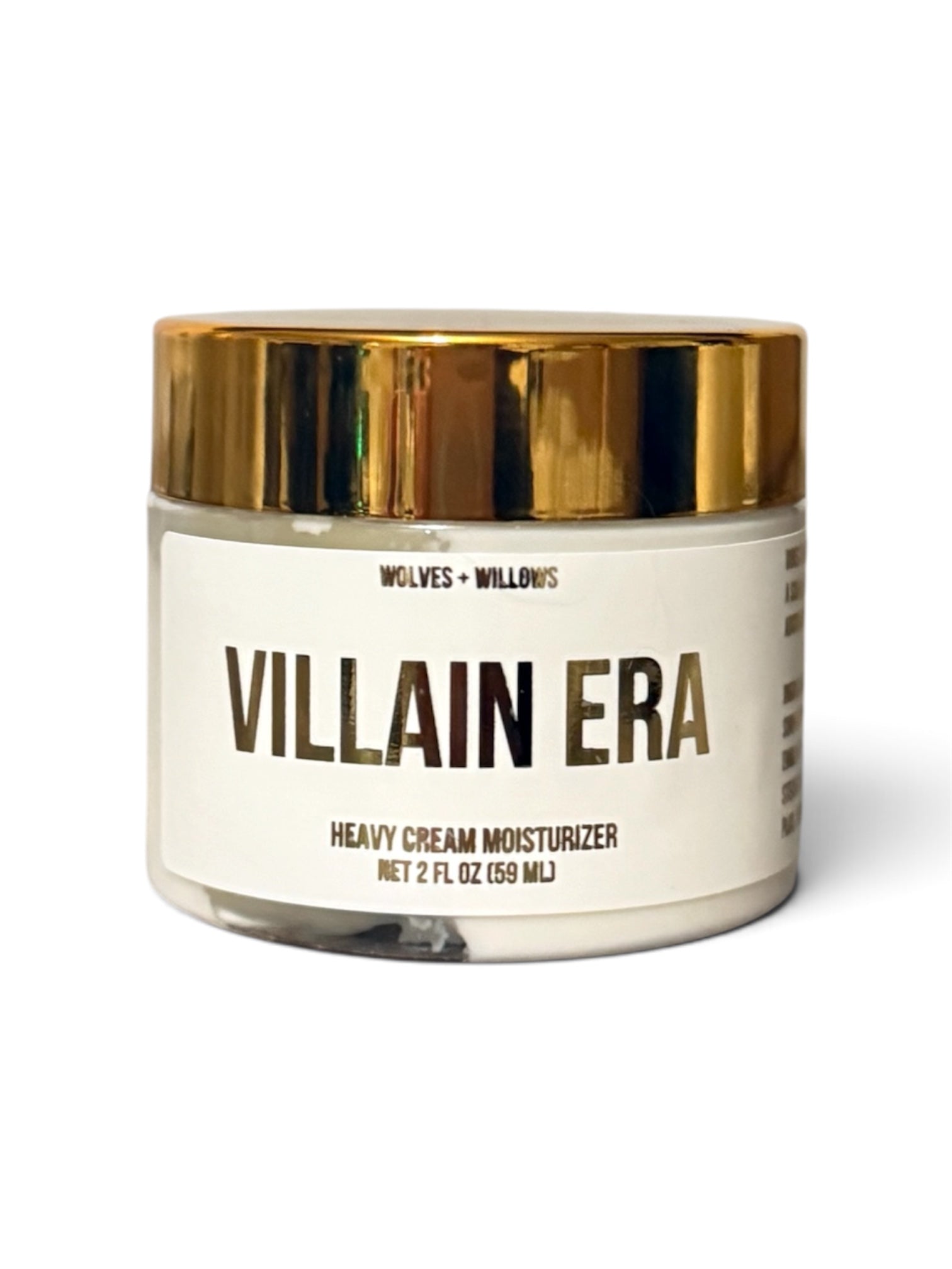 A 2 fl oz jar of Wolves + Willows Villain Era Heavy Cream Moisturizer, featuring a white label with gold lettering and a shiny gold metallic lid, set against a plain white background.